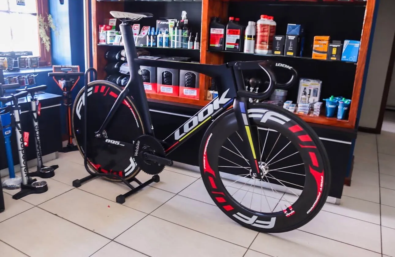 A road bike on a stand in the shop, in front of the parts shelves.