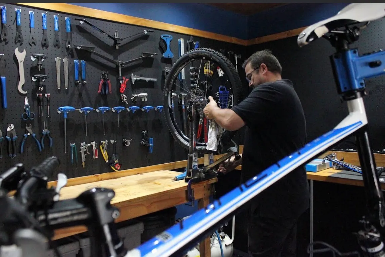 Neil truing a wheel at the workshop bench at Neilson Cycles, in front of a full tool wall.